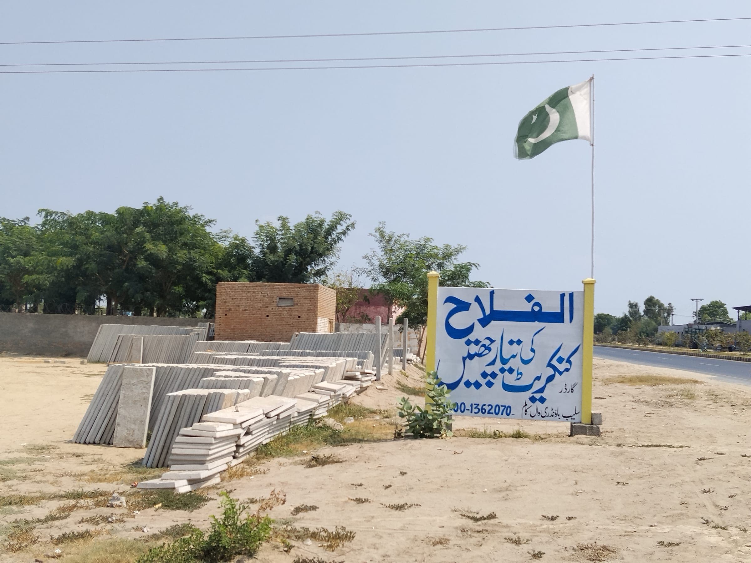 Alfalah Concrete signboard and flag beside stacks of precast concrete roof slabs